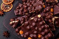 Food, Black bitter chocolate with whole hazelnuts, candied fruits and mint, broken into pieces on a dark concrete background [IBR124773714]