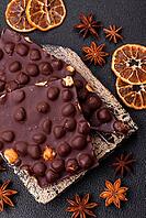 Food, Black bitter chocolate with whole hazelnuts, candied fruits and mint, broken into pieces on a dark concrete background [IBR124773716]