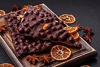 Food, Black bitter chocolate with whole hazelnuts, candied fruits and mint, broken into pieces on a dark concrete background [IBR124773718]