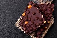 Food, Black bitter chocolate with whole hazelnuts, candied fruits and mint, broken into pieces on a dark concrete background [IBR124773720]