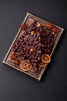 Food, Black bitter chocolate with whole hazelnuts, candied fruits and mint, broken into pieces on a dark concrete background [IBR124773721]