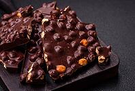 Food, Black bitter chocolate with whole hazelnuts, candied fruits and mint, broken into pieces on a dark concrete background [IBR124773722]