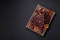 Food, Black bitter chocolate with whole hazelnuts, candied fruits and mint, broken into pieces on a dark concrete background [IBR124773724]