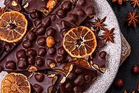 Food, Black bitter chocolate with whole hazelnuts, candied fruits and mint, broken into pieces on a dark concrete background [IBR124773728]