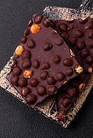Food, Black bitter chocolate with whole hazelnuts, candied fruits and mint, broken into pieces on a dark concrete background [IBR124773730]