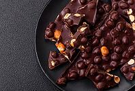 Food, Black bitter chocolate with whole hazelnuts, candied fruits and mint, broken into pieces on a dark concrete background [IBR124773731]