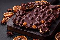Food, Black bitter chocolate with whole hazelnuts, candied fruits and mint, broken into pieces on a dark concrete background [IBR124773732]