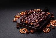 Food, Black bitter chocolate with whole hazelnuts, candied fruits and mint, broken into pieces on a dark concrete background [IBR124773733]