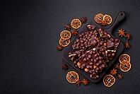 Food, Black bitter chocolate with whole hazelnuts, candied fruits and mint, broken into pieces on a dark concrete background [IBR124773736]