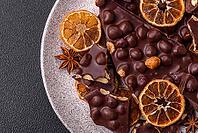 Food, Black bitter chocolate with whole hazelnuts, candied fruits and mint, broken into pieces on a dark concrete background [IBR124773738]