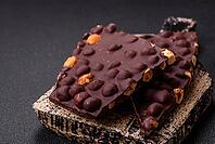Food, Black bitter chocolate with whole hazelnuts, candied fruits and mint, broken into pieces on a dark concrete background [IBR124773739]