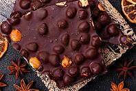 Food, Black bitter chocolate with whole hazelnuts, candied fruits and mint, broken into pieces on a dark concrete background [IBR124773741]