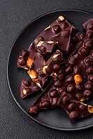 Food, Black bitter chocolate with whole hazelnuts, candied fruits and mint, broken into pieces on a dark concrete background [IBR124773742]