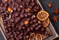 Food, Black bitter chocolate with whole hazelnuts, candied fruits and mint, broken into pieces on a dark concrete background [IBR124773743]