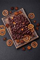 Food, Black bitter chocolate with whole hazelnuts, candied fruits and mint, broken into pieces on a dark concrete background [IBR124773744]
