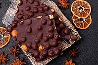 Food, Black bitter chocolate with whole hazelnuts, candied fruits and mint, broken into pieces on a dark concrete background [IBR124773746]