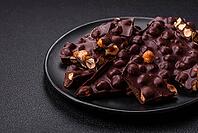 Food, Black bitter chocolate with whole hazelnuts, candied fruits and mint, broken into pieces on a dark concrete background [IBR124773747]