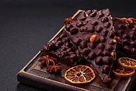 Food, Black bitter chocolate with whole hazelnuts, candied fruits and mint, broken into pieces on a dark concrete background [IBR124773749]