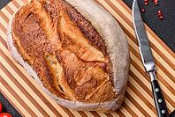 Food, A loaf of brown bread with grains of cereals on a wooden cutting board on a dark concrete background [IBR124773755]