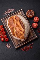 Food, A loaf of brown bread with grains of cereals on a wooden cutting board on a dark concrete background [IBR124773756]