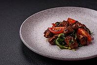 Food, Delicious warm salad with pieces of meat, spinach, tomatoes, salt, spices and herbs on a dark concrete background [IBR124773759]