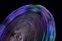 Colourful striped light illuminated spinning ferris wheel in motion moving at night [IBR124817854]