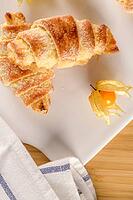 Small croissant with physalis fruits in white ceramic tray, homemade cakes on wooden table top [IBR124817873]