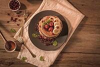 Pancakes with raspberries, banana slices, pomegranate seeds and honey on wooden vintage table [IBR124817897]