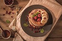 Pancakes with raspberries, banana slices, pomegranate seeds and honey on wooden vintage table [IBR124817898]