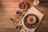 Pancakes with raspberries, banana slices, pomegranate seeds and honey on wooden vintage table [IBR124817901]