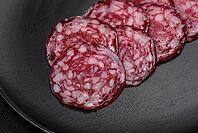Food, Delicious smoked sausage with bacon, salt, spices and herbs cut into slices on a wooden cutting board [IBR124842039]