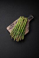 Food, Delicious fresh sprigs of asparagus on a dark textured background. Ingredients for a healthy vegetarian meal [IBR124842066]