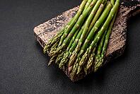 Food, Delicious fresh sprigs of asparagus on a dark textured background. Ingredients for a healthy vegetarian meal [IBR124842074]