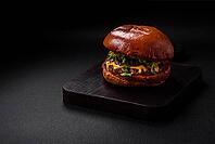 Food, Burger with juicy beef cutlet, cheese, tomatoes, salt, spices and herbs on a dark concrete background [IBR124842080]