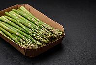 Food, Delicious fresh sprigs of asparagus on a dark textured background. Ingredients for a healthy vegetarian meal [IBR124842097]
