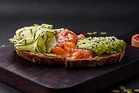 Food, Delicious brown bread toast with salmon, avocado, cucumber and sesame seeds on a textured concrete background [IBR124876418]