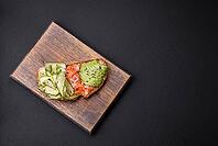 Food, Delicious brown bread toast with salmon, avocado, cucumber and sesame seeds on a textured concrete background [IBR124876421]