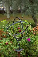 Armillary sphere, which also functions as a sundial or sun clock in a garden surrounded by plants in summer, Loviisa, Finland [IBR124899516]