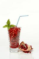 Pomegranate seeds in glass and straw, halved pomegranate [IBR124899853]
