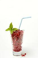 Pomegranate seeds in glass and straw, halved pomegranate [IBR124899867]