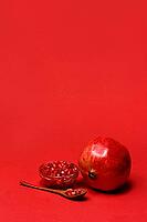 Pomegranate and seeds in wooden spoon and bowl, with red background, Punica granatum [IBR124899869]