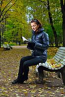 Young woman is sitting on a bench in an autumn park and reading [IBR124906339]