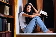 Beautiful woman is sitting on a windowsill and holding a book [IBR124906346]