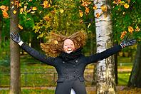 Happy woman is throwing dry autumn leaves in park [IBR124906358]