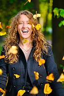 Happy woman is throwing dry autumn leaves in park [IBR124906364]