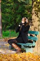 Young woman is sitting on the bench in autumn park and listening music [IBR124906367]