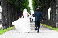 Bride and groom is running with joined hands on city park road [IBR124906369]