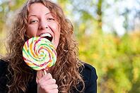Happy woman is eating a big lollipop in park [IBR124906384]