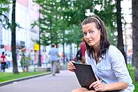 Beautiful woman is sitting in city with laptop and looking at camera [IBR124906396]