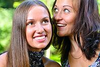 Two female friends are sharing secrets in summer park [IBR124906402]